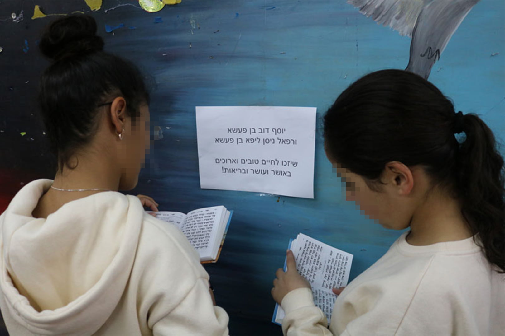 Keren Hayeled students praying near a printed sign with names of orphanage donors to pray for, as part of the Prayer Project at the orphanage