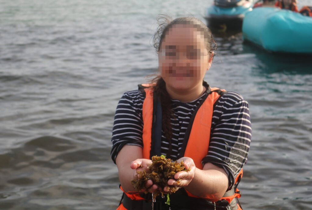 Keren Hayeled student holding a handful of seaweed and wearing a life-jacket on a trip to the beach in Israel