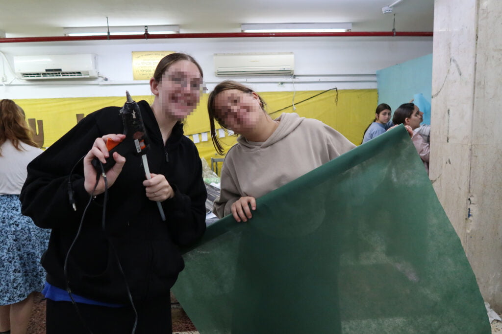 Girls smiling, working on decorating the dining room wall at Keren Hayeled orphanage in Israel