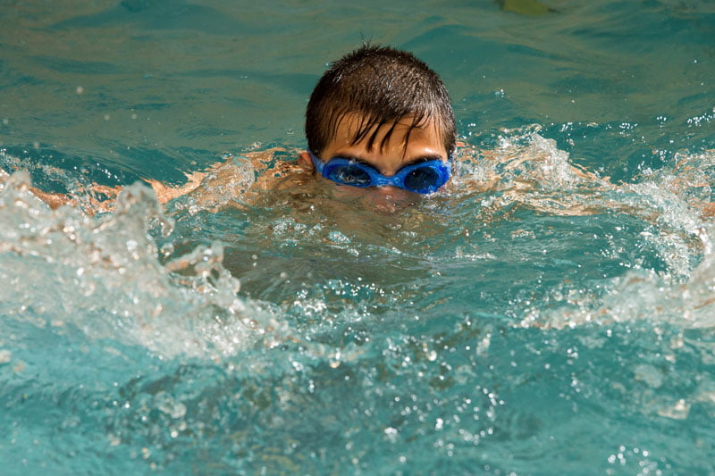 Boy swimming with goggles during invigorating orphanage extracurricular swimming program